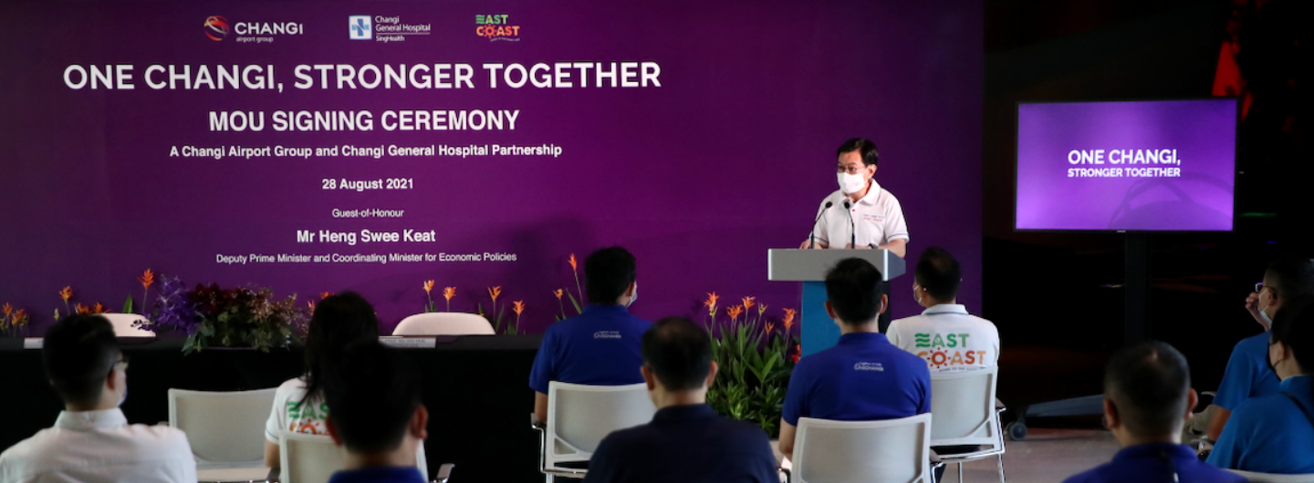 Event with Heng Swee Keat at a podium, "One Changi" backdrop, audience seated.